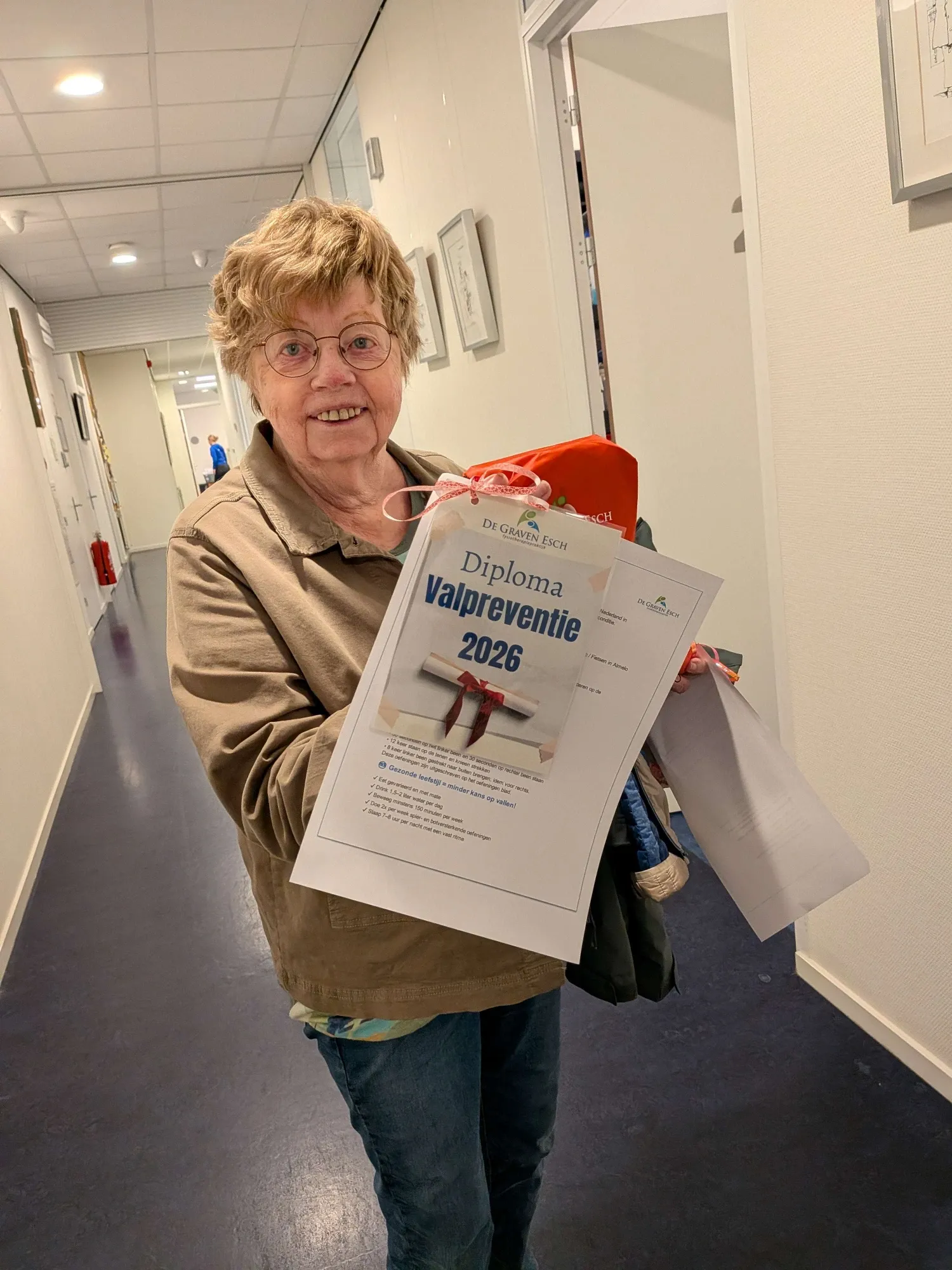 A participant in the corridor of the practice holding her fall prevention diploma and a gift bag